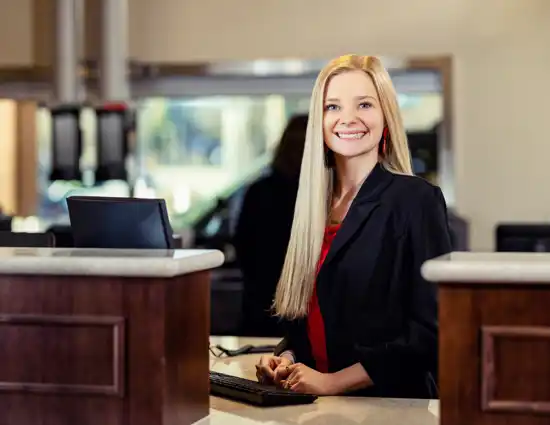 Blonde Woman in red shirt and black blazer smiling behind a computer