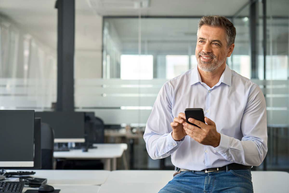 Happy Mid Aged Business Man Using Phone In Office