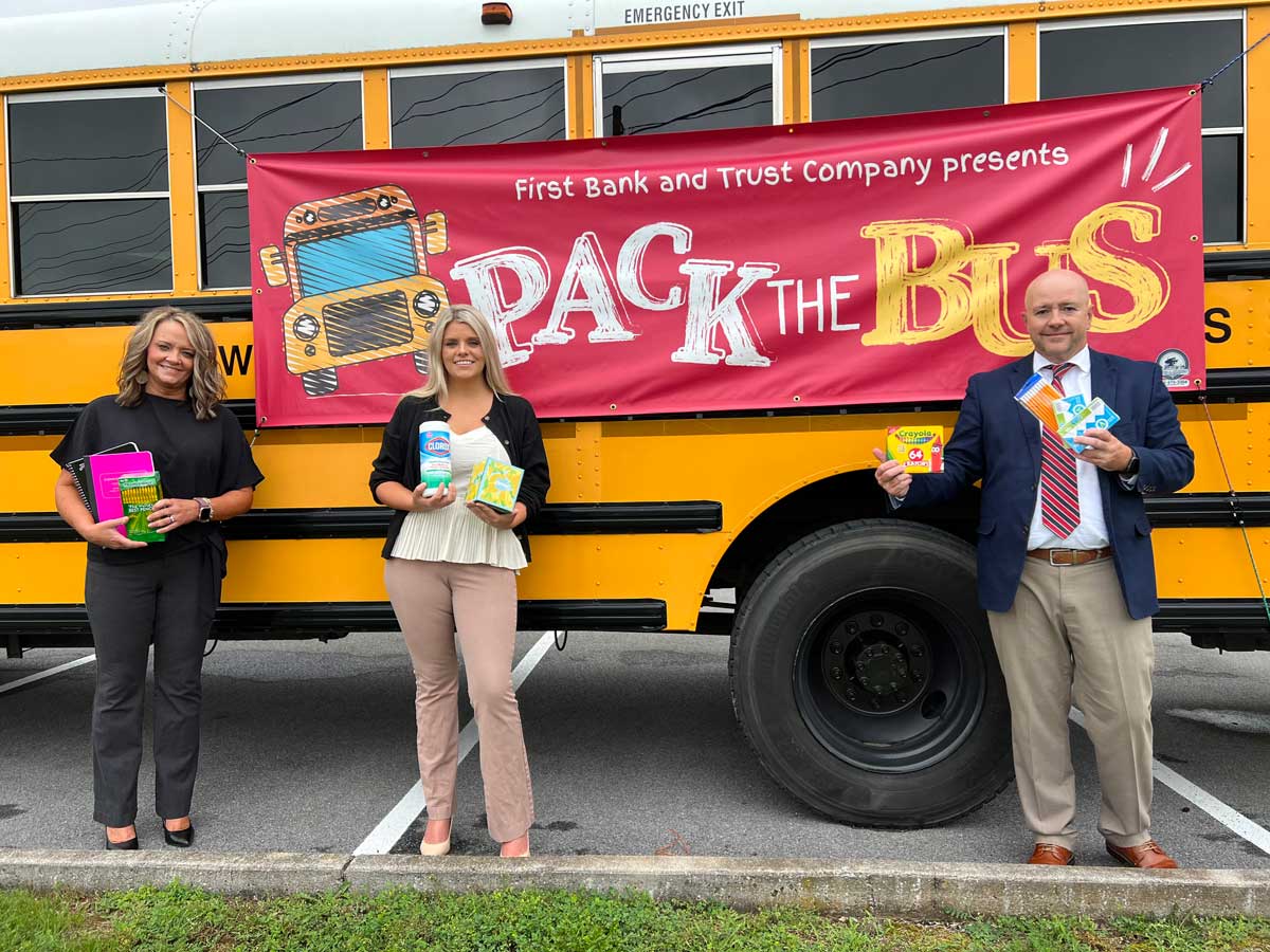 Three People Holding School Supplies In Front Of A Bus