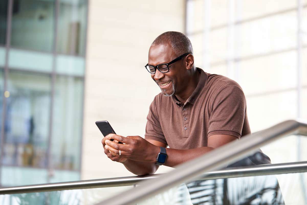 Older Black Man Smiling At His Phone Outside
