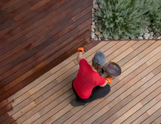 Woman in red shirt brushing dark brown stain on new wooden deck