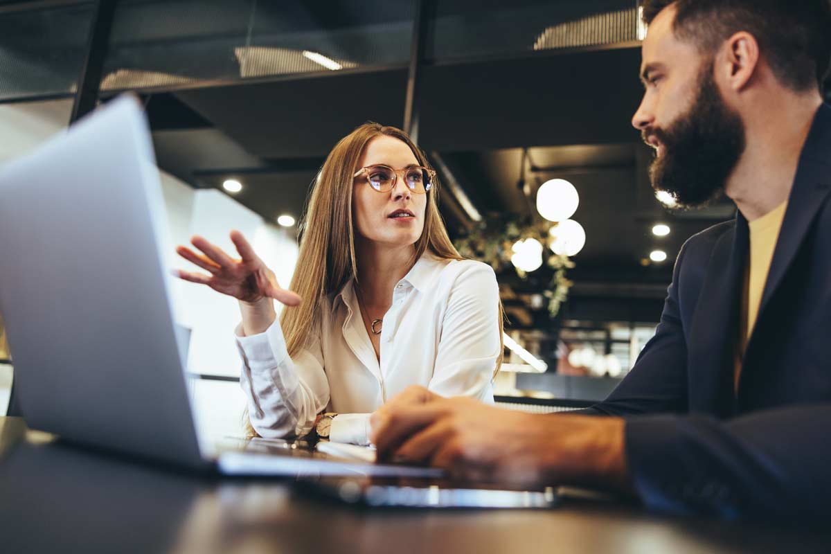 Blonde Woman And Bearded Man Talking Near Laptop
