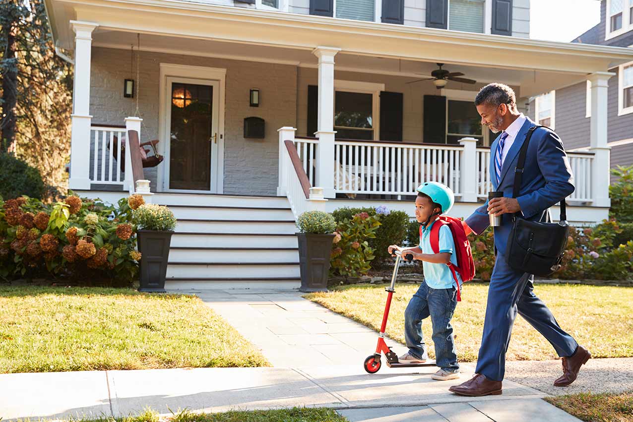 black man in suit walking with scootering son to school