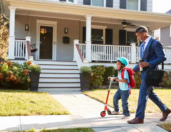 black man in suit walking with scootering son to school
