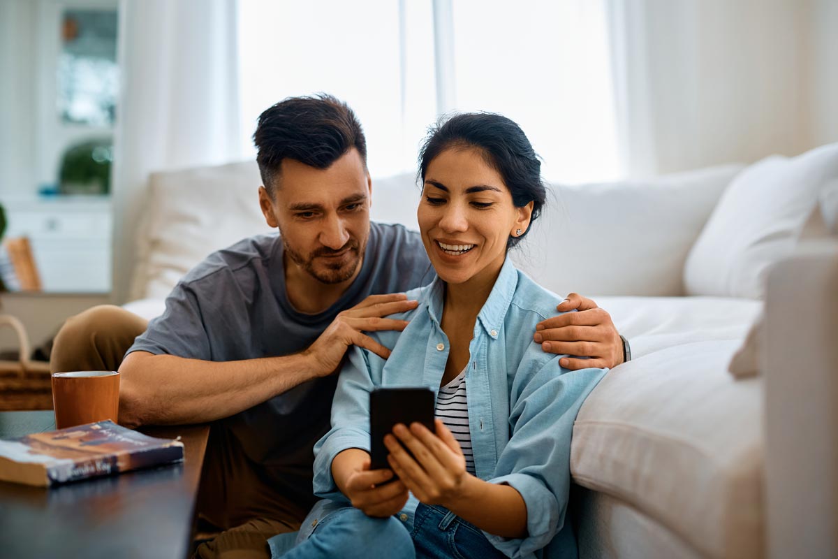 Happy Couple Using Mobile Phone In The Living Room 