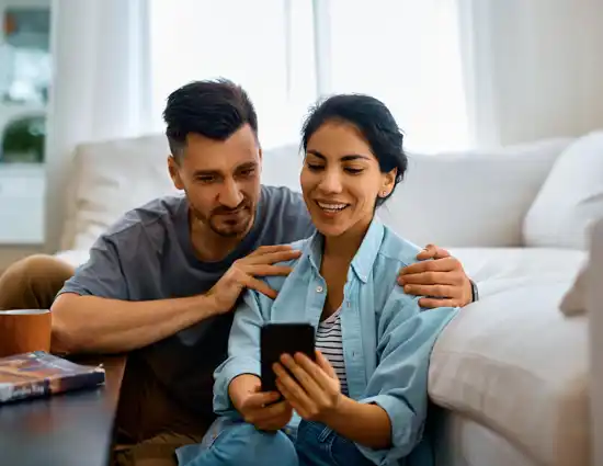 Happy Couple Using Mobile Phone In The Living Room 