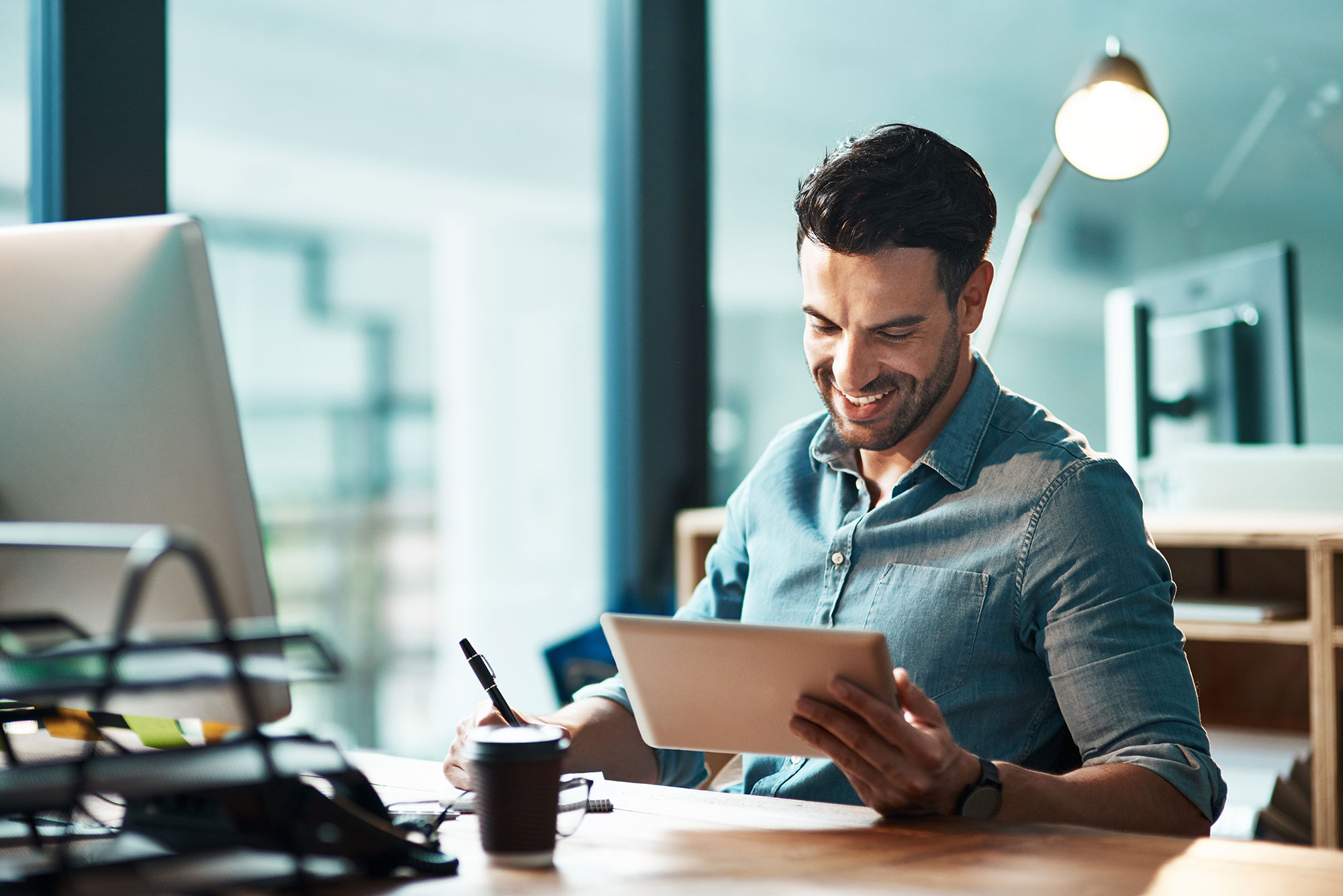 Man sits at computer with tablet in hand
